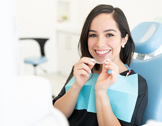 Happy dental patient holding clear aligner close to her mouth